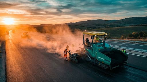 Asphalt paver laying a new tollway lane at sunset